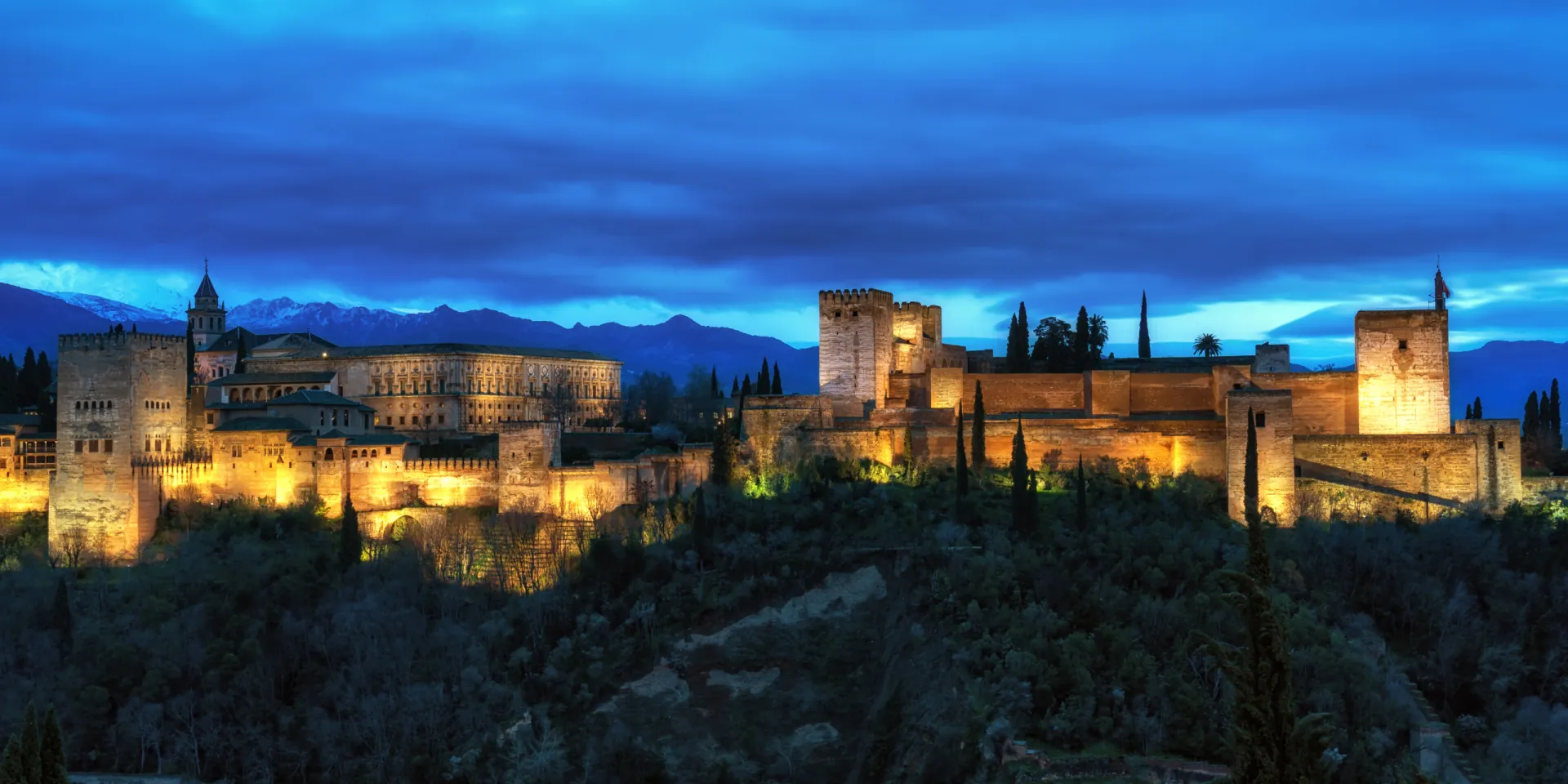 Patio de los Leones iluminado durante la visita nocturna, con las arquerías reflejadas en el suelo mojado